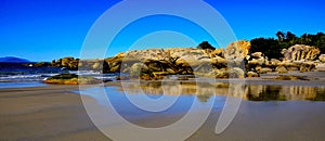 Tranquil, sunny beach with textured rock and reflections