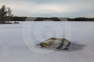 Tranquil winter scenery with a rock in frozen lake