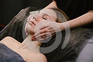 Tranquile woman receiving facial massage in a beauty salon with hands
