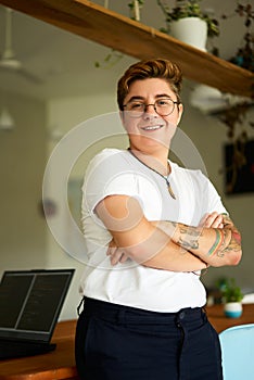 Confident transgender pro in office attire stands with arms folded, smiling at camera. Trans exec in well-lit workspace photo