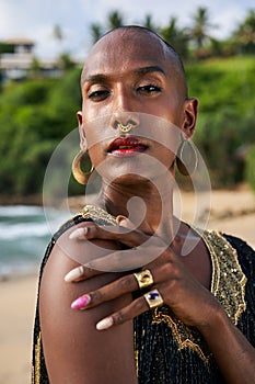 Trans sexual ethnic fashion model with brass jewelry accessories in elegant posture looks at camera. Epatage gay black