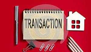 TRANSACTION text written on a notebook with pencils and office tools and model wooden house