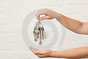 Transfer of house key on a white brick background. Woman's hands with bunch of keys