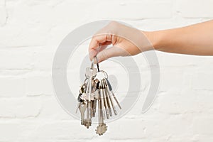 Transfer of house key on a white brick background. Woman's hands with bunch of keys
