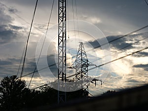 Transformer line tower against a cloudy sunset. In foreground there isa tower with ham radio antenna