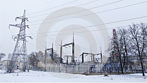 A transformer substation with a metal power line tower, ceramic insulators, and lightning rods is located on a snow-covered lawn a