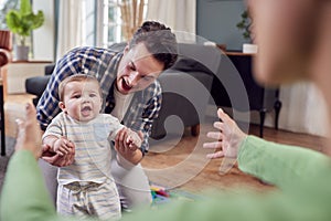 Transgender Family Encouraging Baby To Take First Steps In Lounge At Home