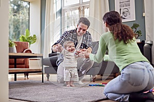 Transgender Family Encouraging Baby To Take First Steps In Lounge At Home