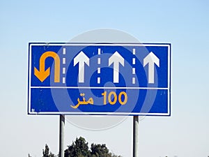 Translation of Arabic (100 M one hundred meters) at a side informative traffic sign board showing 4 lanes and directing