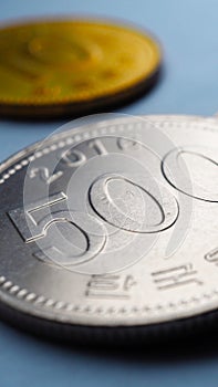 Translation: Bank of Korea. Korean coins lie on blue paper surface. 500 won coin close-up. Vertical stories illustration about