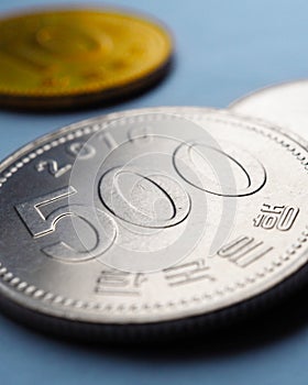 Translation: Bank of Korea. Korean coins lie on blue paper surface. 500 won coin closeup. Vertical stories illustration about