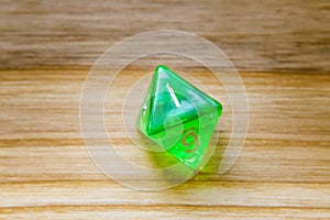 A translucent green eight sided playing dice on a wooden background with number one on a top