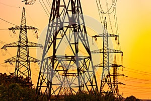 Transmission lines on background of industry electricity towers. Sunset silhouette high voltage electric towers.