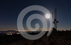 Transmission masts on a high mountain under a full moon with the illuminated coastline. photo