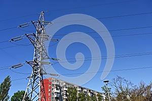 A transmission tower and high voltage wires on the background of a residential building