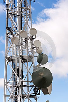 Transmitters and aerials on telecommunication tower with cloudy blue sky