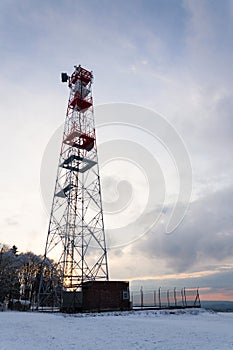 Transmitters and aerials on telecommunication tower, sunset in snowy country