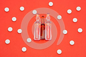 Transparent ampoules with liquid medicine are on red background around tablets which form polka dots pattern. Concept photo of com