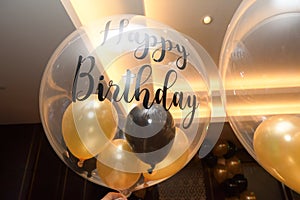 A transparent balloon with smaller yellow and black balloons inside and the words Happy Birthday printed on it