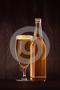 Transparent beer bottle and glass weizen with golden lager on dark brown wood board, vertical, mock up.