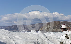 Transparent blue ice hummocks on lake Baikal shore. Siberia winter landscape view with lighthouse. Snow-covered ice of