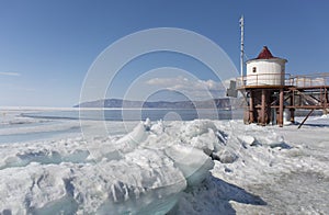 Transparent blue ice hummocks on lake Baikal shore. Siberia winter landscape view with lighthouse. Snow-covered ice of