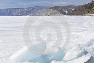 Transparent blue ice hummocks on lake Baikal shore. Siberia winter landscape view. Snow-covered ice of the lake. Big