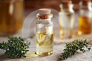 A transparent bottle of aromatherapy essential oil with fresh thyme on a table