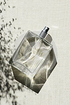 Transparent bottle of perfume on light grey fabric background. Women's and men's essence.