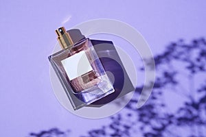 Transparent bottle of perfume on a lilac background. Fragrance presentation with daylight.