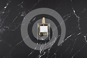 Transparent bottle of perfume with spray on black marble surface.