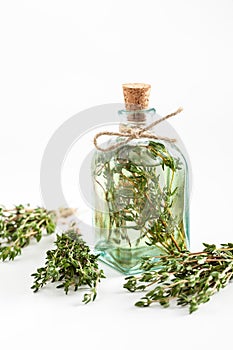 Transparent bottle of thyme essential oil or infusion and healing herbs