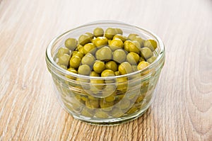 Transparent bowl with green peas on table