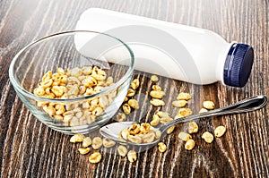 Transparent bowl with puffed wheat, bottle of yogurt, puffed wheat, spoon on wooden table