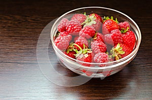 Transparent bowl with strawberries and raspberries on a brown wooden background