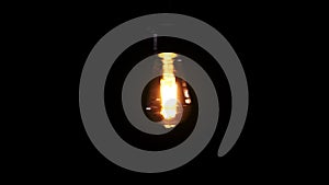 Transparent Classic Bulb Hanging on Wire and Flickering on Black Background