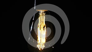 Transparent Classic Bulb Hanging on Wire and Flickering on Black Background