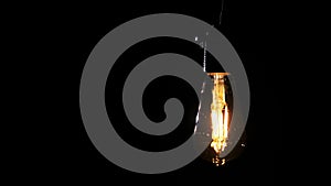 Transparent Classic Bulb Hanging on Wire and Flickering on Black Background