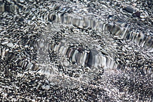 Transparent clear calm water surface with small grey pebbles sea bottom texture
