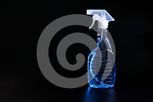 Transparent container with a spray bottle and light blue disinfectant liquid stands against a black background. The concept of