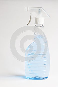 Transparent container with a spray bottle and light blue disinfectant liquid on a white background. Cleanliness, disinfection and