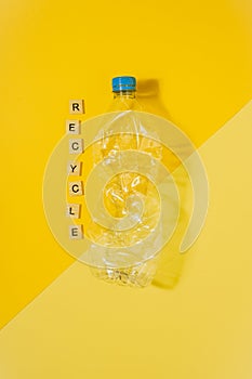 Transparent and crushed plastic bottle with blue cap on a yellow background and the word recycle. Recycling and environment