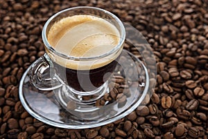 A transparent cup with aromatic frothy coffee stands on the beans. Close-up