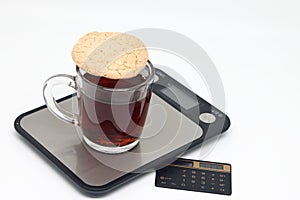 A transparent cup of black tea stands on a kitchen electronic scale, counting calories