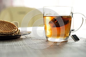 Transparent cup with brewed tea bag is on the table next to the plate