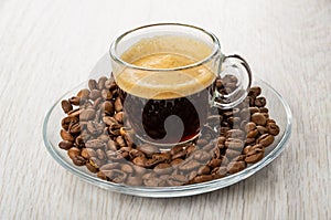 Transparent cup with coffee espresso in saucer with coffee beans on table