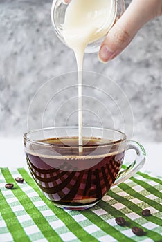 Transparent cup of coffee with pouring condensed milk