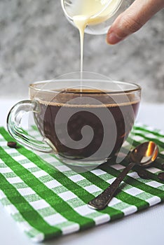 Transparent cup of coffee with pouring condensed milk