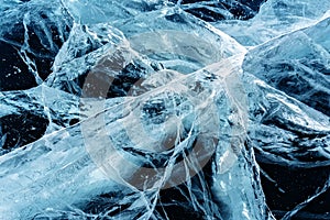 Transparent dark blue ice of frozen Baikal lake with white cracks pattern.