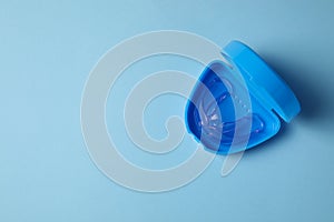 Transparent dental mouth guard in container on light blue background, top view with space for text. Bite correction